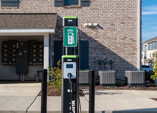 A black electric vehicle charging station sits in front of a brick building.
