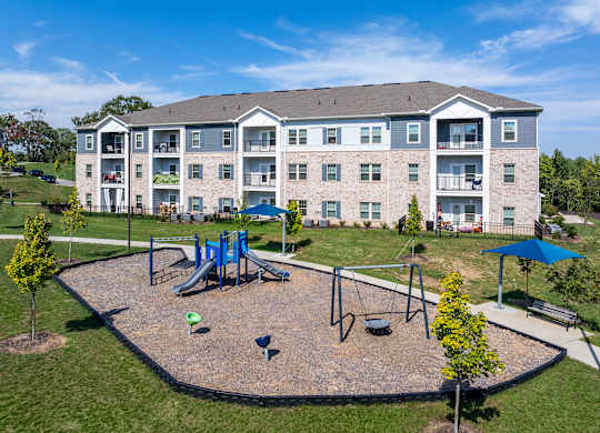 A playground area is located in front of a large apartment building.
