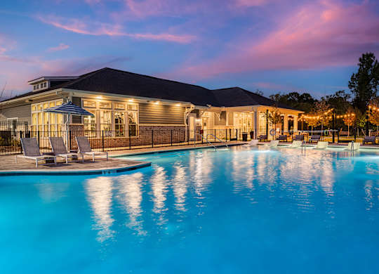 A large swimming pool in front of a house with lights strung up around the pool area.