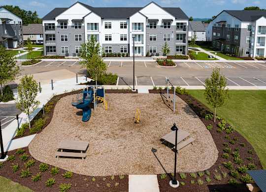 A playground area with a slide, swings, and a bench in front of apartment buildings.