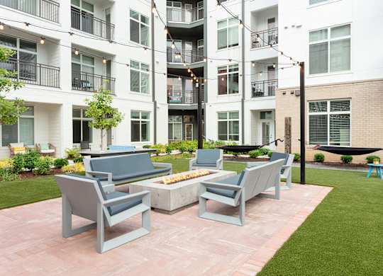 an outdoor patio with chairs and a fire pit in front of an apartment building