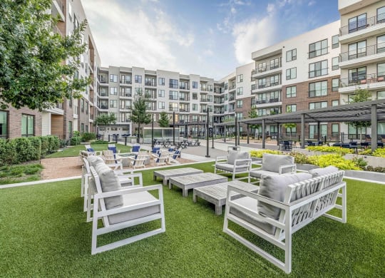 an outdoor lounge area with white chairs and lawn furniture in front of an apartment building