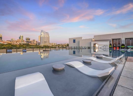 a rooftop pool with lounge chairs and a view of the city