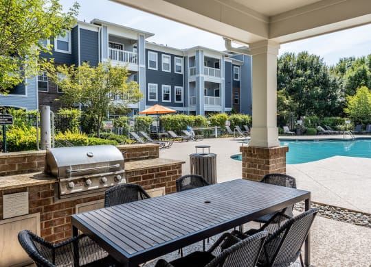 a patio with a grill and table and chairs and a swimming pool in the background