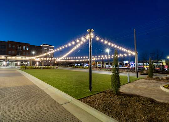 a city street at night with a string of lights over a grassy area