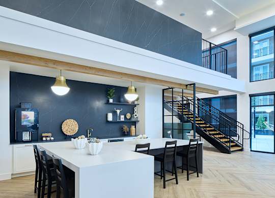 A modern kitchen with a white island and black chairs.