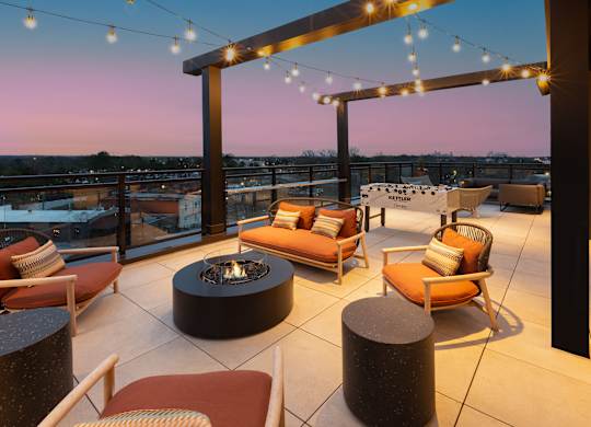 A patio with a fire pit and chairs under string lights.