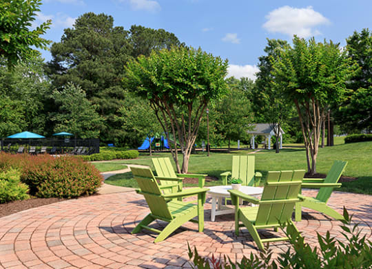 a group of green adirondack chairs on a brick patio with trees in the background