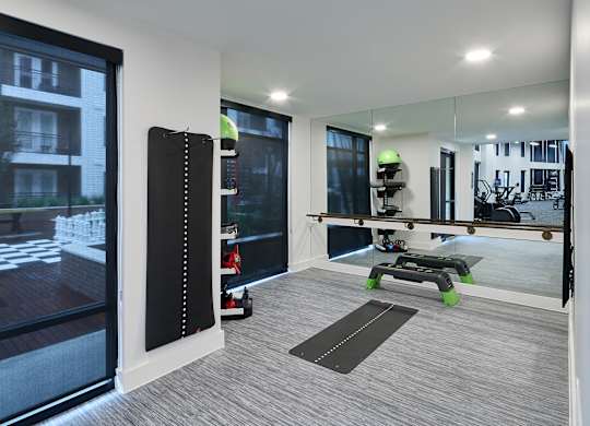 A modern room with a large mirror, a yoga mat, and a view of a building outside.