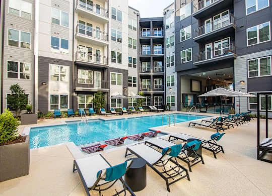 an outdoor pool with lounge chairs and tables at an apartment building