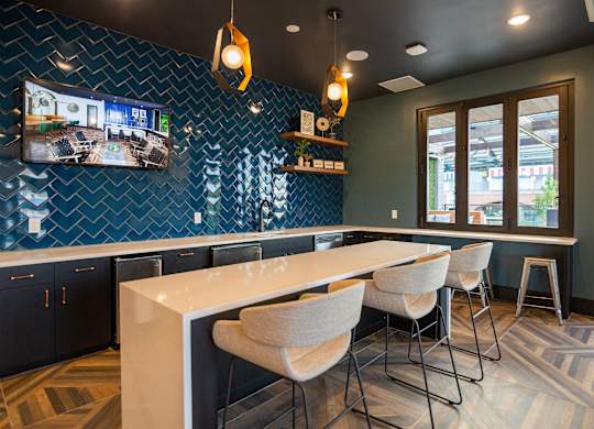 a kitchen with a long counter and chairs and a tv on the wall