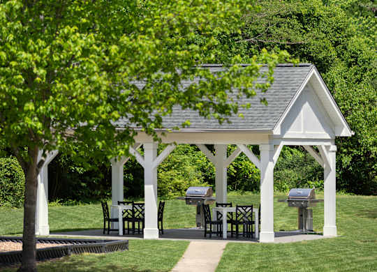 A white gazebo with a table and chairs is surrounded by greenery.