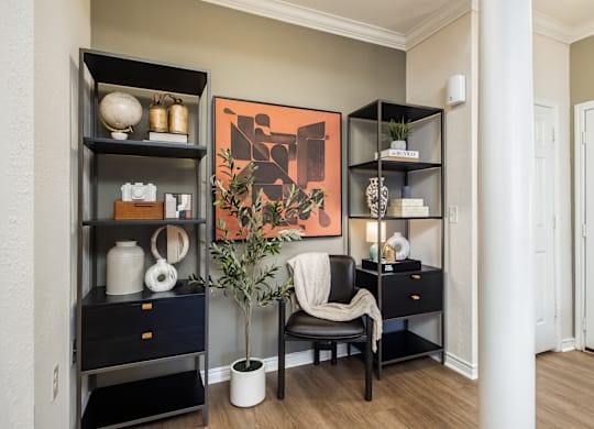 A room with a chair, a plant, and a shelf with decorative items.