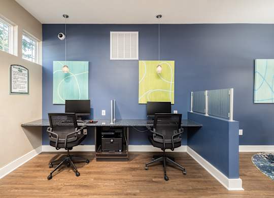 Two black chairs are in front of a desk with a laptop and a monitor.