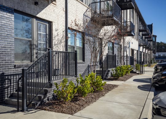 front view of a brick apartment building with stairs and a sidewalk