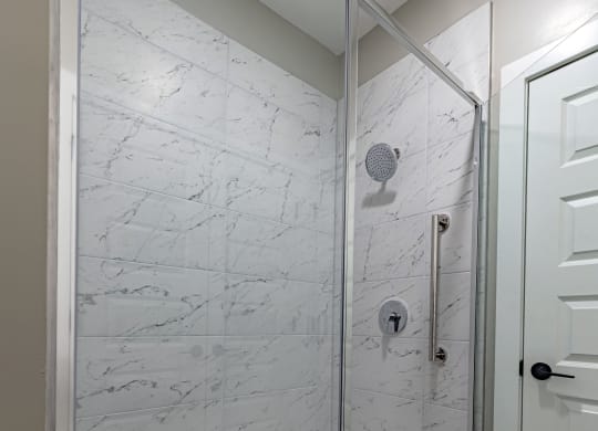 the master bathroom has a large shower with marble walls and wood flooring