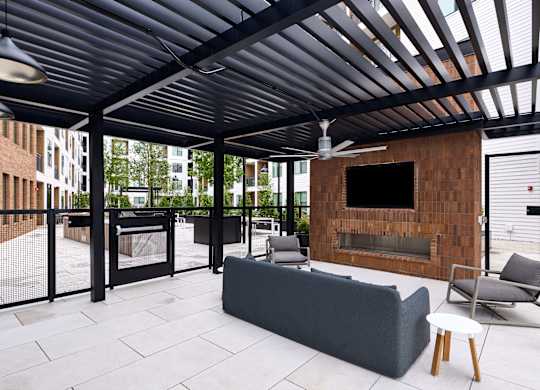 A patio with a grey couch, a fireplace, and a ceiling fan.