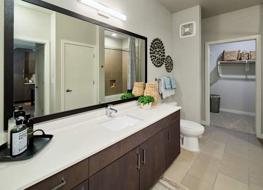 A bathroom with a large mirror, a sink, and a toilet.