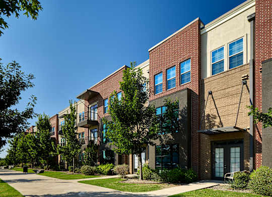 A row of apartment buildings with trees in front.