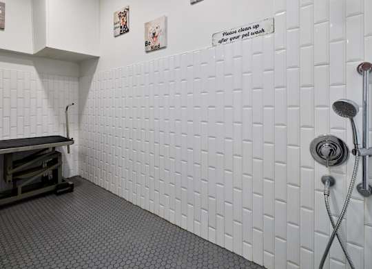 A white tiled bathroom with a shower head and a sign on the wall.
