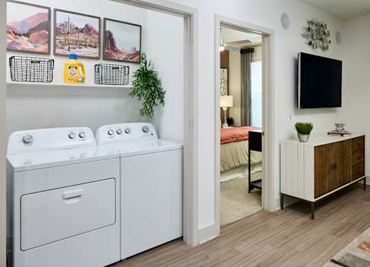 A white washing machine and dryer in a small room with a TV and a plant.