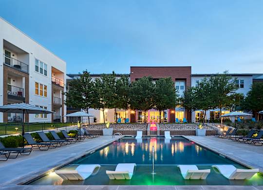 A swimming pool surrounded by lounge chairs and umbrellas in a residential area.