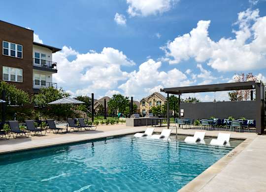 A swimming pool with lounge chairs and umbrellas in front of a building.