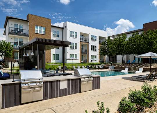 A sunny day at a poolside with a barbecue grill and lounge chairs.