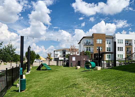A playground with a slide and swings is surrounded by a fence and apartment buildings.