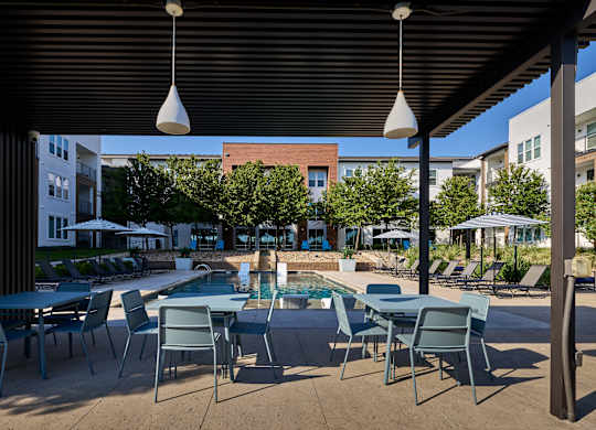 A pool area with chairs and tables is shaded by a black awning.