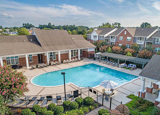 A swimming pool surrounded by a black fence and a building with a brown roof.