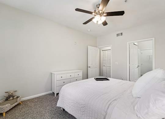 A white bedroom with a bed, dresser, and ceiling fan.