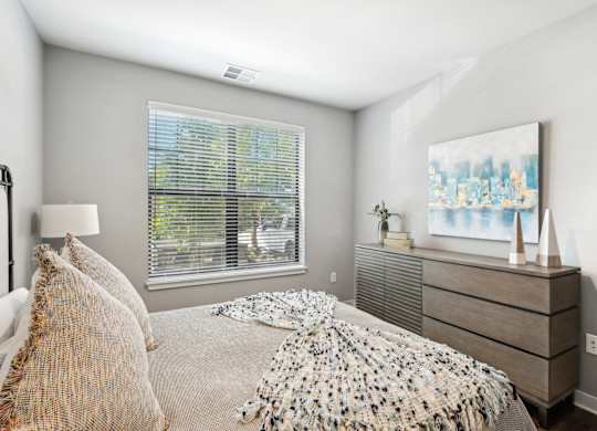 A bedroom with a bed, a nightstand, and a window with blinds.
