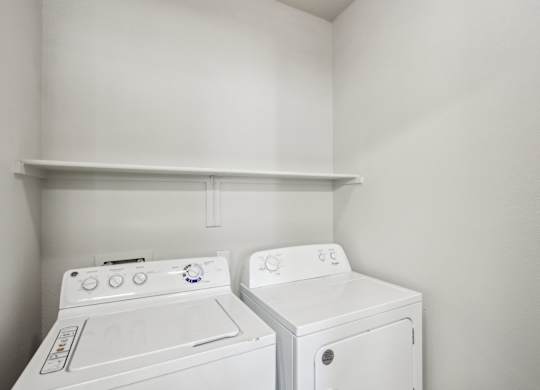 Two white front loading washing machines in a small laundry room at Sweetwater At Metro North Apartments, Phoenix, AZ 85029