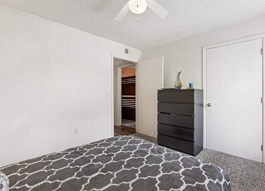 A bedroom with a bed, dresser, and ceiling fan.
