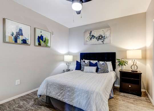 A bedroom with a bed, nightstand, and two wall art pieces at Sweetwater At Metro North Apartments, Phoenix, AZ 85029