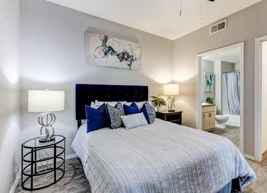 A bedroom with a bed, nightstand, and a painting on the wall at Sweetwater At Metro North Apartments, Arizona