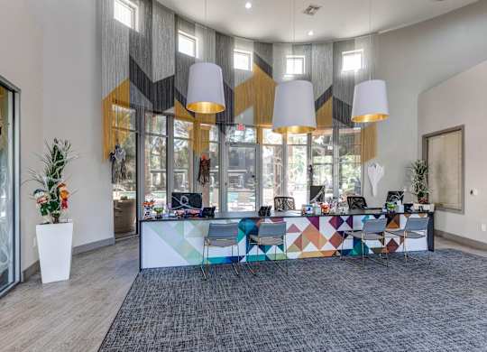 A modern office space with a colorful reception desk and a view of the outside through the glass doors at Sweetwater At Metro North Apartments, Phoenix  85029