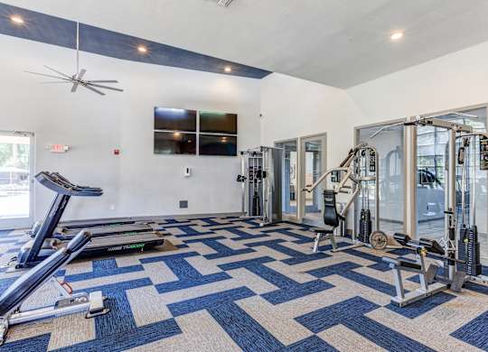 A spacious gym with a variety of equipment and a blue and white patterned carpet at Sweetwater At Metro North Apartments, Phoenix