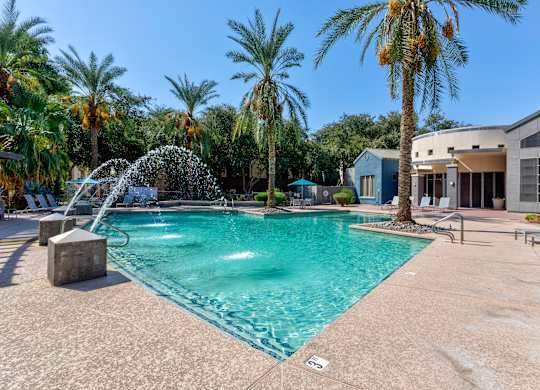 A pool with a waterfall and palm trees in the background at Sweetwater At Metro North Apartments, Arizona 85029