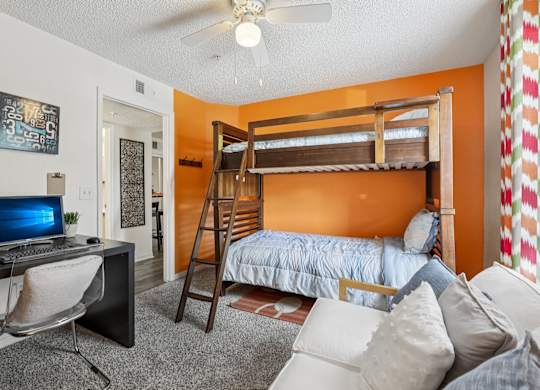 A room with a bunk bed, a desk with a computer, and a chair.