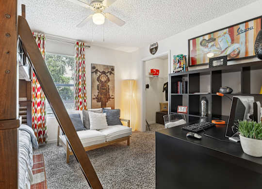 A living room with a couch, a chair, a desk, and a bookshelf.