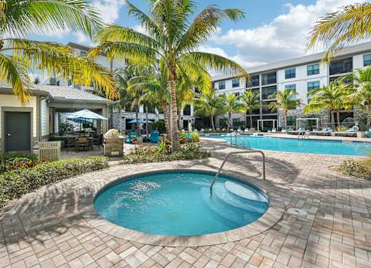 A small pool surrounded by palm trees and a building in the background.