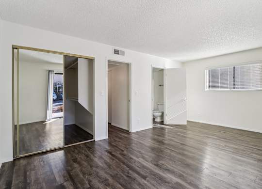 A large empty room with wooden floors and a large mirror on the wall.