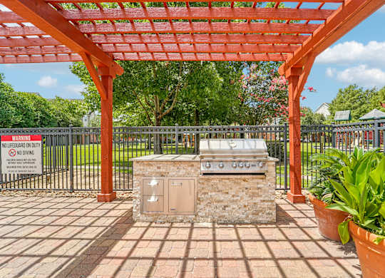 A red pergola is over a stone structure in a park.