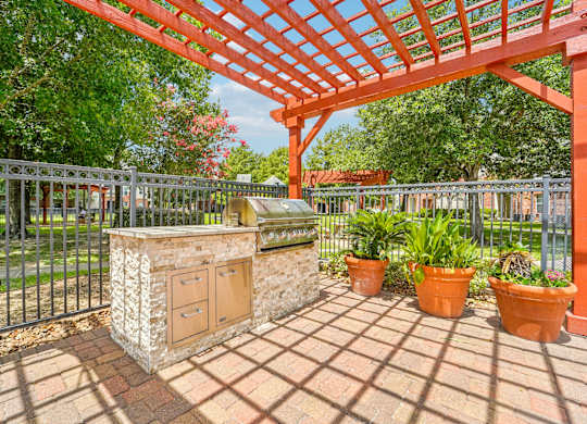 A red pergola is over a stone pillar with potted plants on a brick patio.