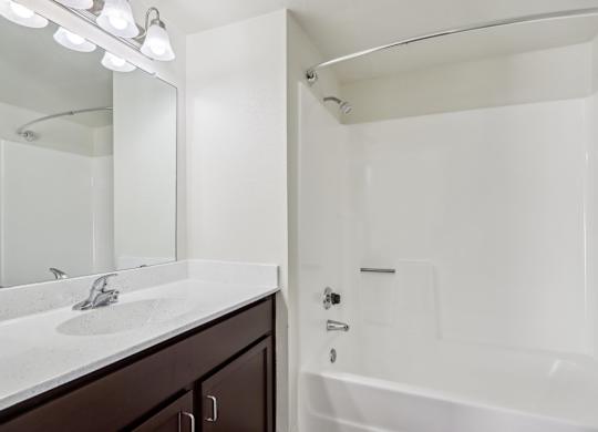 A white bathroom with a sink, mirror, and bathtub.
