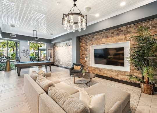 A living room with a large couch and a flat screen TV mounted on a brick wall.
