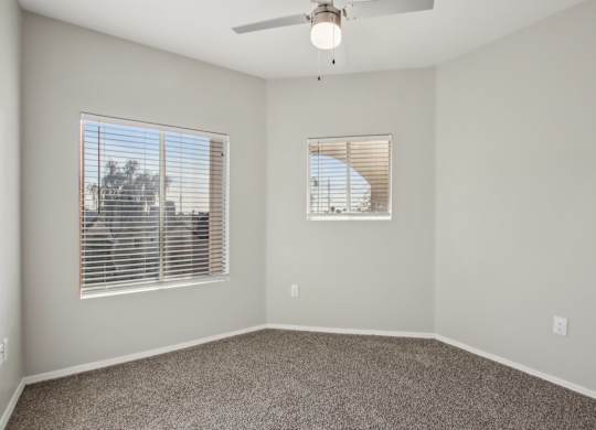 A room with a ceiling fan and two windows at Sweetwater At Metro North Apartments, Phoenix
