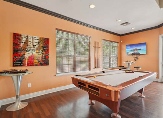 A pool table in a room with a TV mounted on the wall.